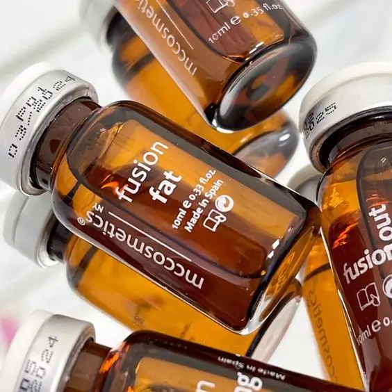 Close-up of amber glass vials filled with liquid, labeled "fusion fat," made in Spain. The vials, promoting optimal health, are positioned at various angles, with white caps and text printed on the glass.