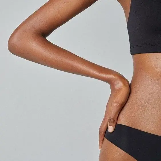 A person is shown from the neck to the hips, wearing a black sports bra and black underwear, with one arm bent and a hand resting on the hip. The plain gray background emphasizes a focus on overall wellness, subtly hinting at holistic approaches to address issues like hormonal imbalance.