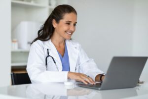 Mature doctor using laptop at clinic, telemedicine concept