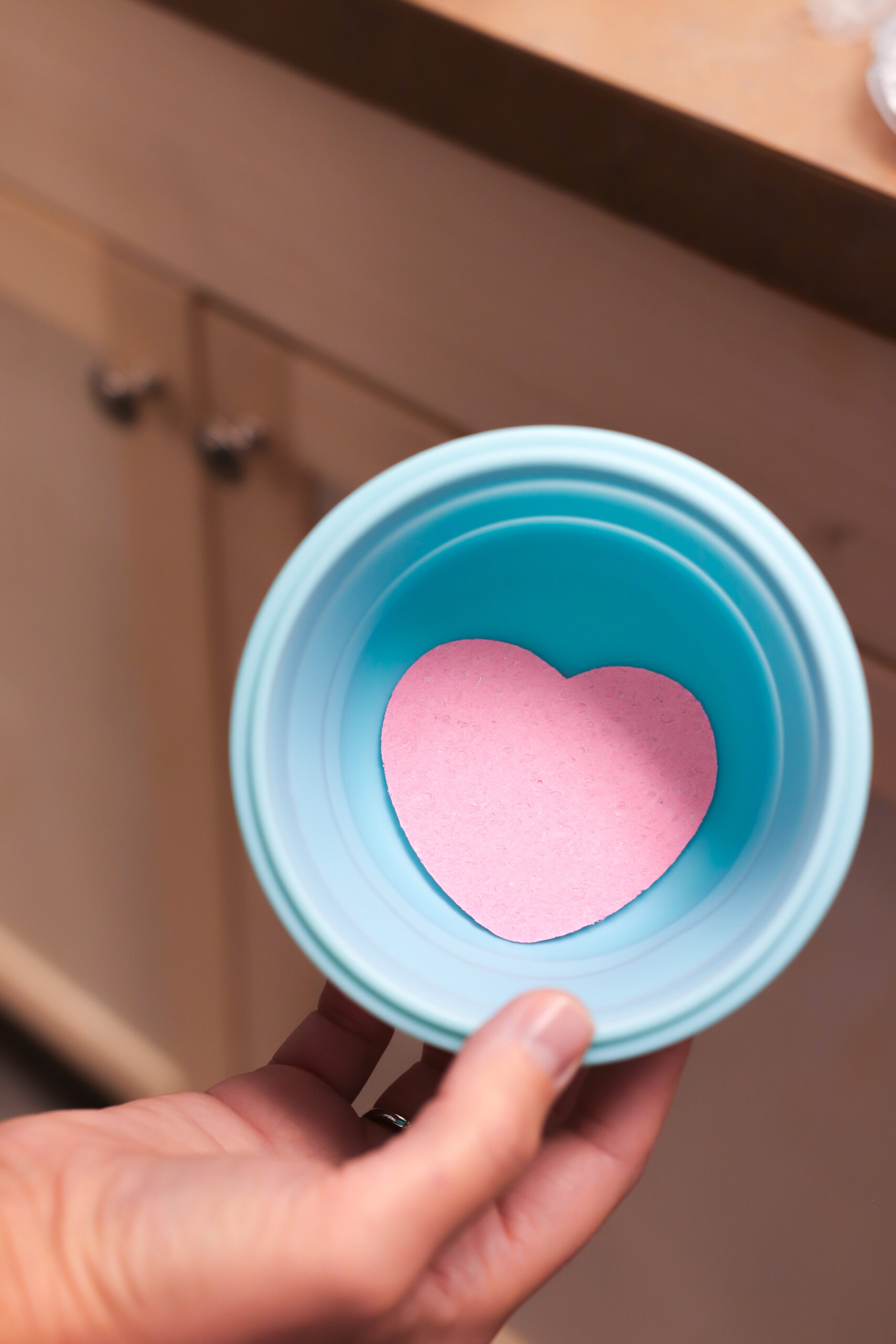 A hand holds a turquoise bowl with a pink heart-shaped object inside, symbolizing the heart's role in functional medicine.