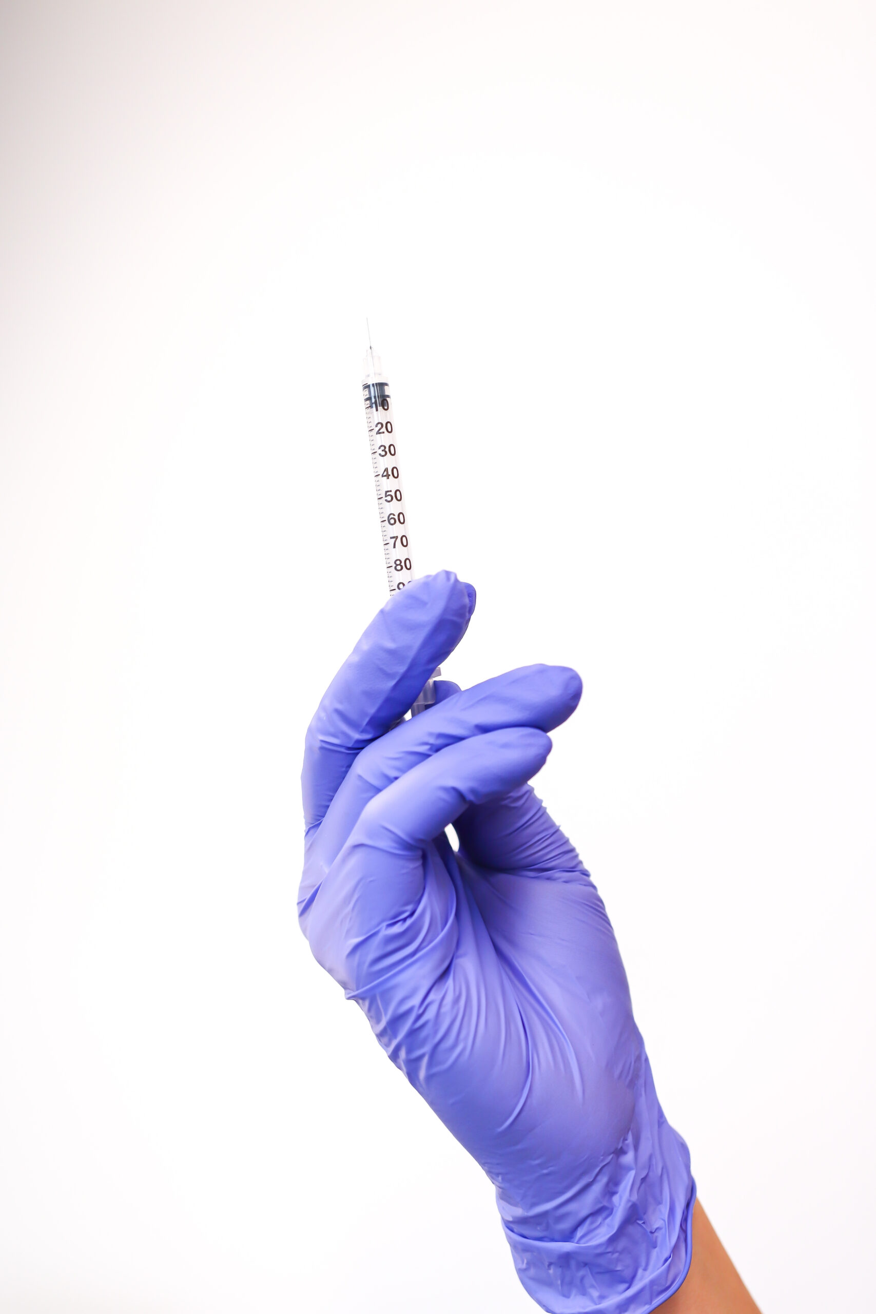 A hand in a purple glove holding a syringe, emphasizing the role of hormone therapy in modern health and wellness, set against a plain white background.