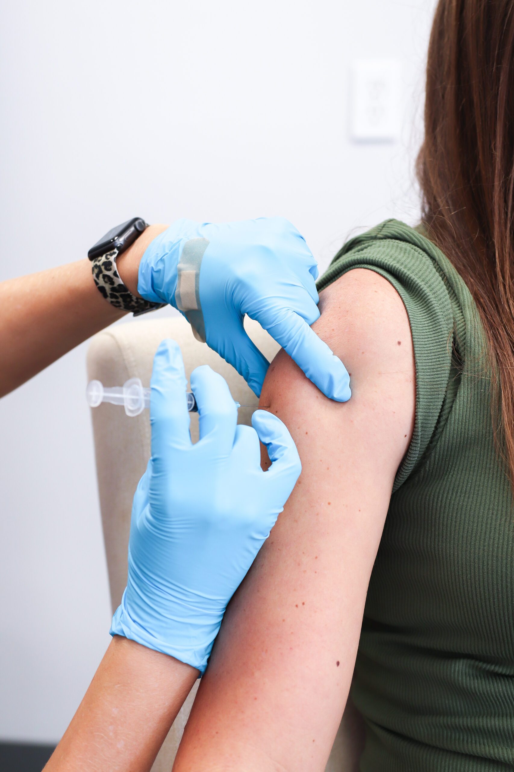 A person in a green shirt is receiving a vaccine in the upper arm from a healthcare worker wearing blue gloves, promoting health and wellness.