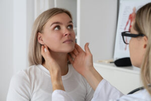 A healthcare professional examines a patient's neck in a medical setting.