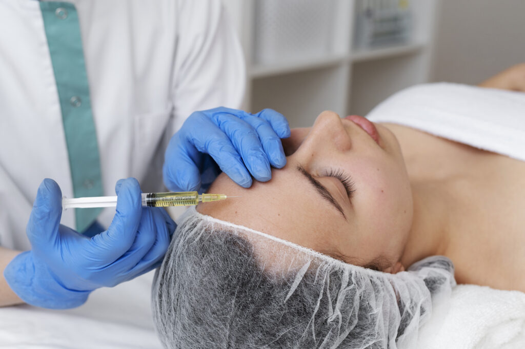 A person receives an injection in the forehead at a clinic. The person administering the injection wears blue gloves. The patient has a hairnet on.